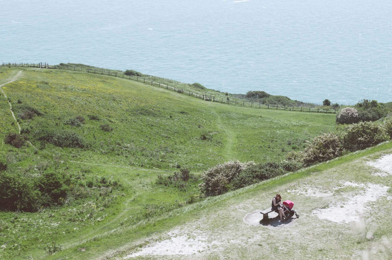 A top view of the Dover cliff layers, starting with a woman sitting on a bench all the way to the ocean at the bottom